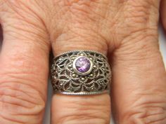 This vintage sterling silver ring features a beautiful round amethyst stone set in a wide open filigree design. The band is adorned with marcasite accents and has a ring size of 7. The ring is perfect for those who appreciate the unique and timeless beauty of vintage jewelry. The purple color of the amethyst stone adds a touch of elegance and sophistication to any outfit. This ring is a perfect addition to any jewelry collection and is sure to make a statement. Jewelry items come in a gift box and are then carefully packaged in a bubble mailer. Everything ships within 48 hours. Tracking is provided. I take great care in packaging so that my items make it safely to their new homes! I also use recycled materials whenever possible. Please pass it on by reusing what you receive from me. Please Ornate Filigree Ring Stamped 925, Ornate Silver Amethyst Ring, Vintage Sterling Silver Rings, Filigree Design, Bubble Mailer, Amethyst Stone, Wide Bands, The Purple, Statement Jewelry