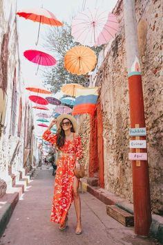 a woman in an orange dress and hat walking down the street with umbrellas overhead