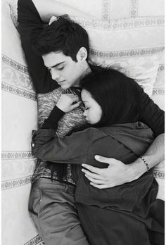 black and white photograph of two people laying on a bed with their arms around each other