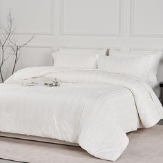 a bed with white comforter and pillows in a room next to a vase on the floor