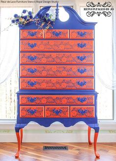 an orange and blue dresser sitting in front of a window with flowers on the top