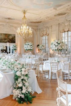 an elegant wedding reception with white flowers and greenery on the tables in front of chandeliers