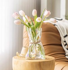 a glass vase filled with pink tulips on top of a wooden side table