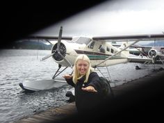 a woman poses in front of an airplane on the water