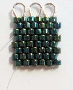 three pieces of green beaded fabric on a white surface with two hooks attached to them