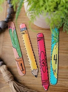 three pencils with numbers painted on them sitting next to a potted plant and beads