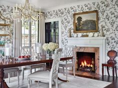 a dining room table with chairs and a fire place in the fireplace, surrounded by floral wallpaper