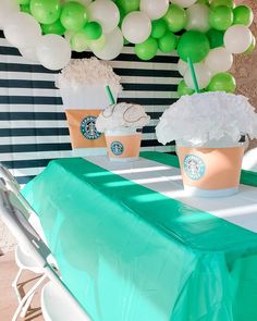 two starbucks cups are sitting on a table with green and white balloons