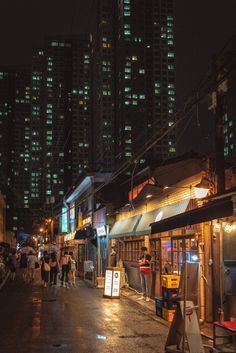 people walking down the street at night in front of some tall buildings with neon lights