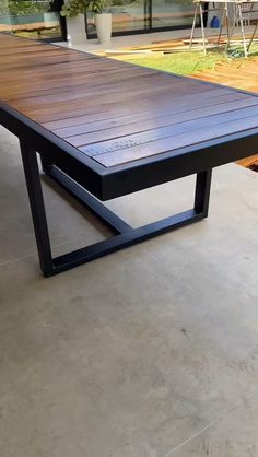 a wooden table sitting on top of a cement floor next to a potted plant