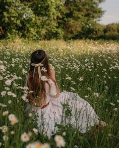 a woman sitting in the middle of a field with daisies on her head and wearing a white dress