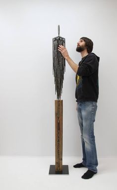 a man standing next to a tall sculpture made out of metal rods and wood sticks