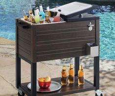 an outdoor bar cart with drinks on it next to a swimming pool and water feature