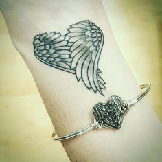 a woman's arm with an angel wing tattoo on it and a heart charm attached to the wrist