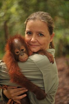 a woman holding a baby oranguel in her arms and smiling at the camera