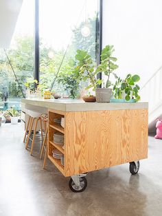 a kitchen island cart with plants on it in front of a window and stairs leading up to the second floor