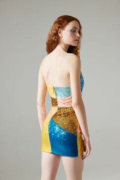 a woman with red hair wearing a blue and yellow sequined dress, looking off to the side