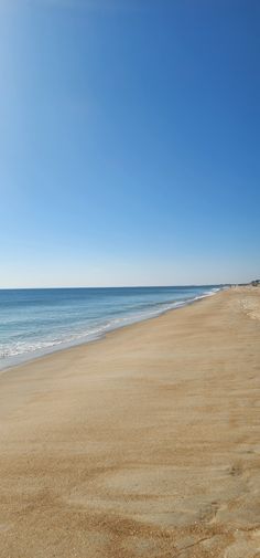 an empty beach with the ocean in the background and blue skies above, on a sunny day