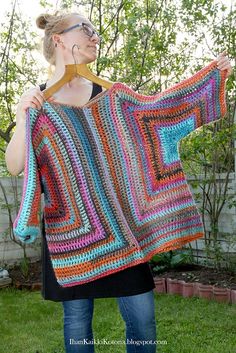 a woman holding up a colorful crocheted blanket