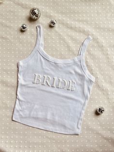 Fully Customizable Bride Crop Top and/or Bridesmaid Crop tank! Please provide the words you would like in the customize box (Mrs. Smith/Wifey/Babes)  if you would like Bride please add Bride or No custom.   These crop tops are handmade by us (Alexandra and Amanda)! The shirt is a polyester cotton blend allowing for a very form fitted yet comfortable style.  These come true to size. So please size accordingly :) The size chart in photos will help with the perfect fit. Pro tip: try measuring your Bachelorette Tank Tops, Custom Text Fitted Summer Tops, Fitted Summer Tops With Custom Text, Summer Fitted Tops With Custom Text, White Custom Text Top For Wedding, Sleeveless Cotton Top For Wedding, Customizable Sleeveless Tops, Bride Tee Shirts, Bridesmaid Tank Tops