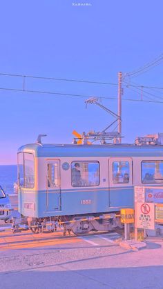 a blue train car sitting on the side of a road next to the ocean with power lines above it