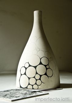 a white vase sitting on top of a table next to a tabletop with an abstract design