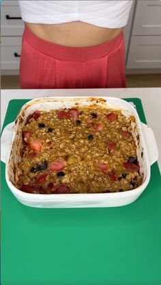 a woman standing in front of a green table with a pan of baked oatmeal