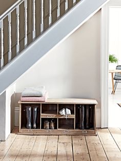 an entryway with wooden flooring and white walls, under a stair case filled with boots