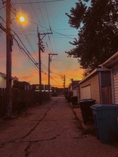 the sun is setting over an alley way with trash cans and garbage cans on either side