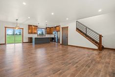 an empty living room with hard wood floors and white walls on the far wall is a large open kitchen