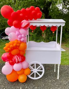 an ice cream cart with balloons attached to the front and sides, sitting on top of gravel