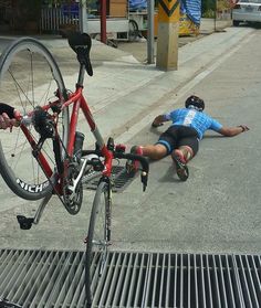 a man laying on the ground next to a bike and another person pushing it up