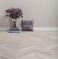 a vase filled with purple flowers sitting on top of a wooden floor next to two books