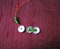 two white buttons with green beads are on a red surface next to an orange string