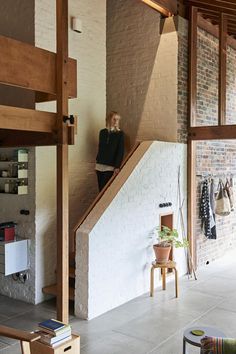 a woman is standing on the stairs in a room with brick walls and wood beams