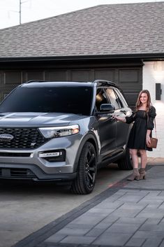 a woman standing next to a silver ford suv in front of a garage with her hand on the door handle