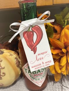 a bottle of hot sauce with a tag on it next to flowers and pumpkins