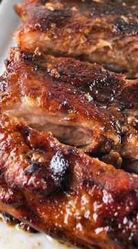 two pieces of meat sitting on top of a white plate covered in bbq sauce