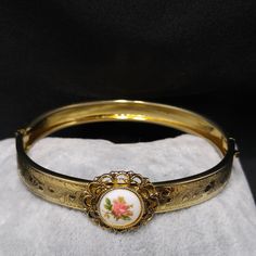 *Description: This is a beautiful repousse gold plated hinged bracelet with a filigree circular porcelain hand painted pink rose accent piece on the top of the bracelet. The bracelet looks beautiful and the gold is bright and shiny. It would make a great vintage gift or a wonderful addition to your vintage jewelry collection. *Approximate Measurements: Length around inside - 6 1/2 Inches, Width - 5/8 Inch *Condition: Great vintage condition. Will see signs of wear under magnification. *Hallmark: Vintage Enamel Jewelry For Anniversary, Vintage Hinged Bangle Gift, Vintage Hinged Bangle As Gift, Vintage Gold Enamel Bracelets, Vintage Hinged Bracelets For Gift, Vintage Cameo Jewelry In Enamel, Vintage Cameo Enamel Jewelry, Vintage Enamel Bangle Jewelry, Vintage Enamel Cameo Jewelry