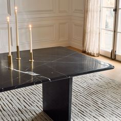 a black marble dining table with gold candles on the top and white rug in front