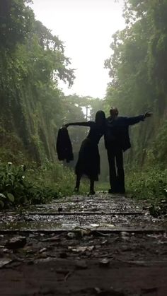 two people standing in the middle of a forest with their arms spread out to each other