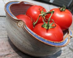 four tomatoes in a blue and white bowl on a wooden table with the tops still attached