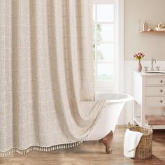 a white bath tub sitting next to a sink under a bathroom window covered in a beige shower curtain