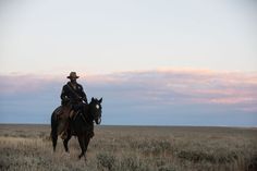 a man riding on the back of a brown horse across a dry grass covered field