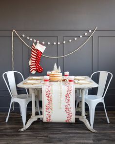 a christmas table setting with stockings hanging on the wall and two white chairs around it