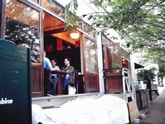 two people sitting at a table in the open window of a small building with lots of windows