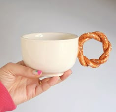 a hand holding a bowl with pretzels in it and a cup next to it