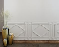 two vases sitting on the floor in front of a wall with white paneling