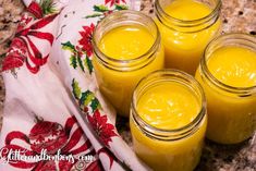 four jars filled with yellow liquid sitting on top of a marble counter next to a red and white towel