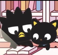 two black cats sitting next to each other in front of a book shelf with books on it